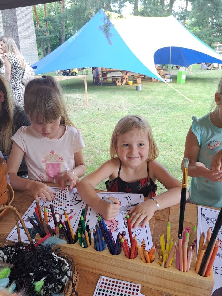 Bērni zīmē un darbojas radošajā darbnīcā zem telts brīvā dabā