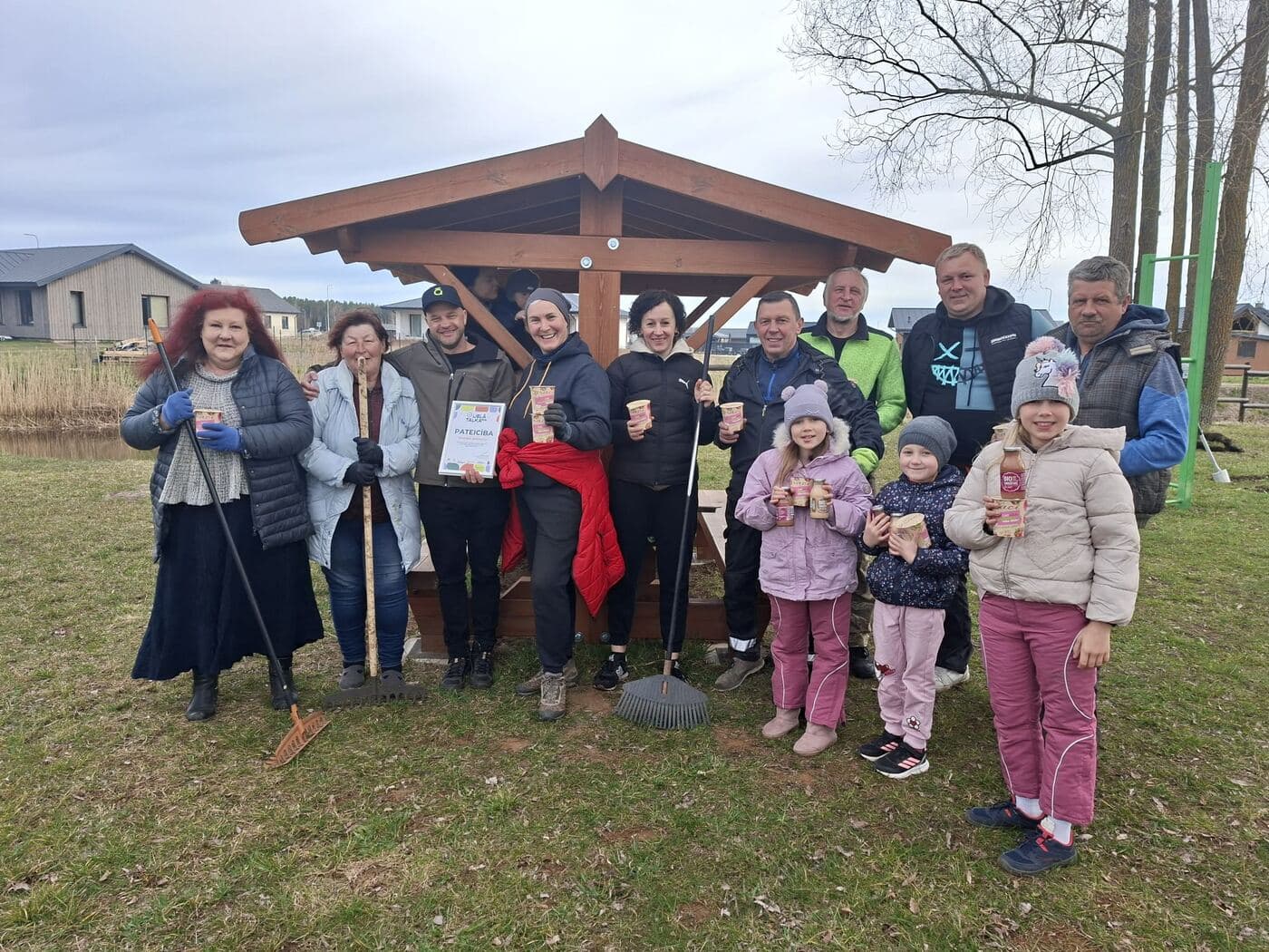 Biedrības biedri ar darbarīkiem pie kopīgi uzceltās lapenes